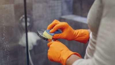 Persona limpiando la cal del cabezal de la ducha con una esponja y guantes
