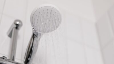 Alcachofa de ducha moderna con agua cayendo en un baño con azulejo blanco
