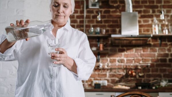 Mujer sirviendo agua de una jarra de cristal en un vaso en una cocina